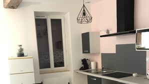 Een moderne keuken met een eethoek, voorzien van een glazen tafel, zwarte stoelen, een inbouwoven en een hanglamp.