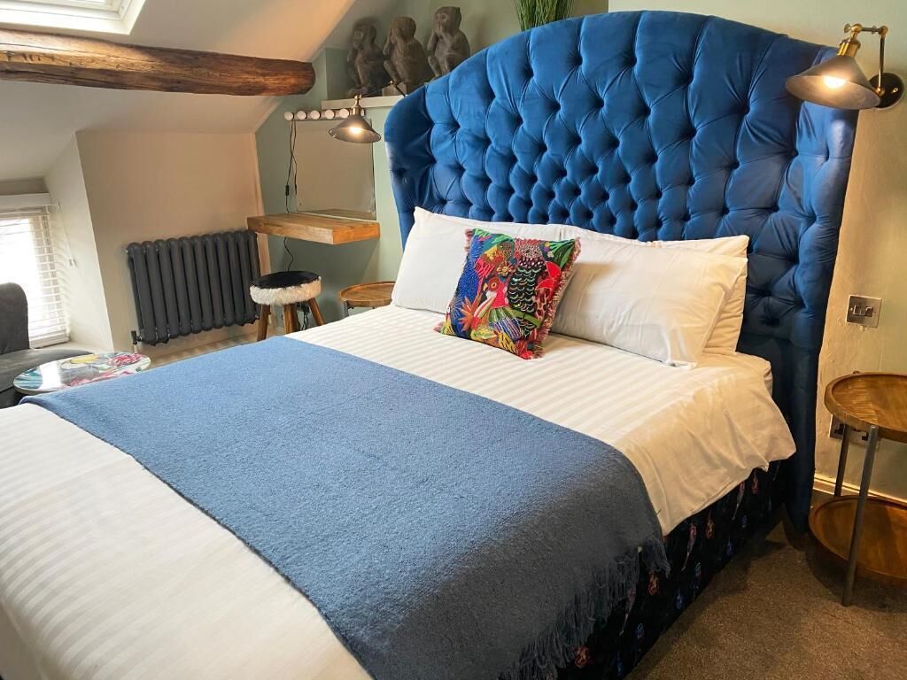 Un dormitorio con un cabecero azul capitonado, ropa de cama blanca y una almohada colorida.