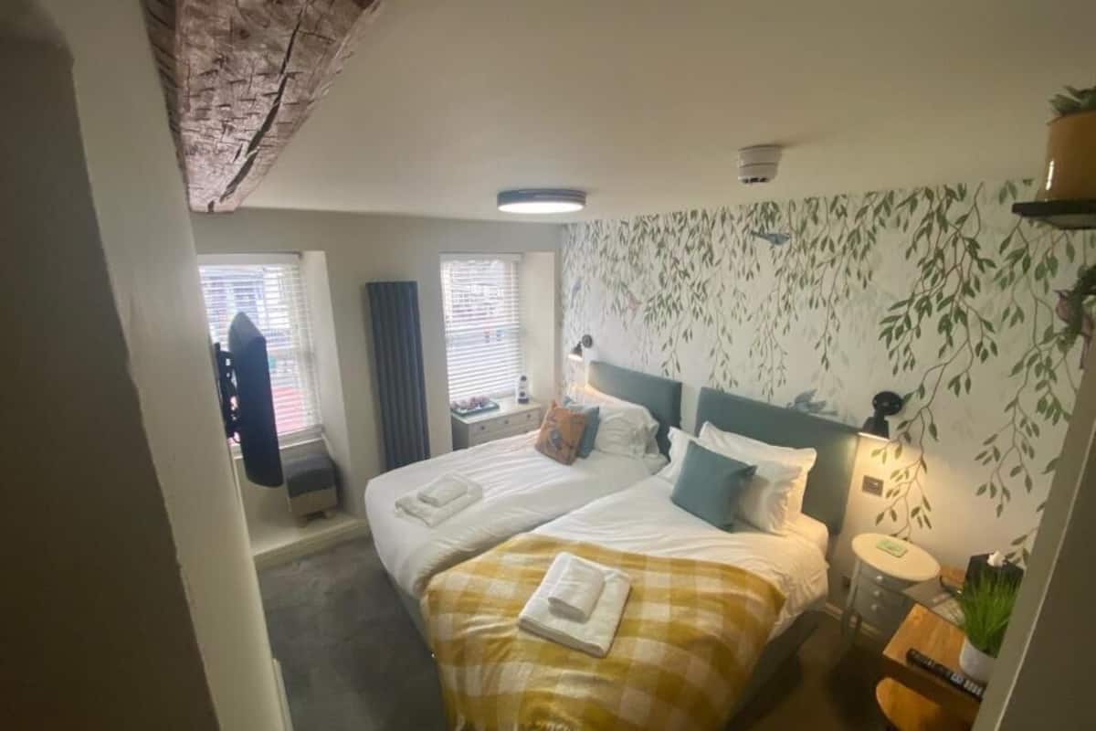 Habitación de hotel con dos camas, una mesita, una silla, una lámpara y una ventana con persianas.