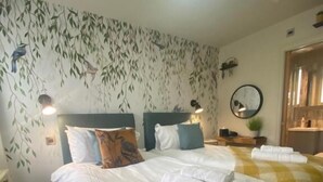 Una camera d'albergo con due letti, un grande specchio e una parete decorata con un motivo a foglia.
