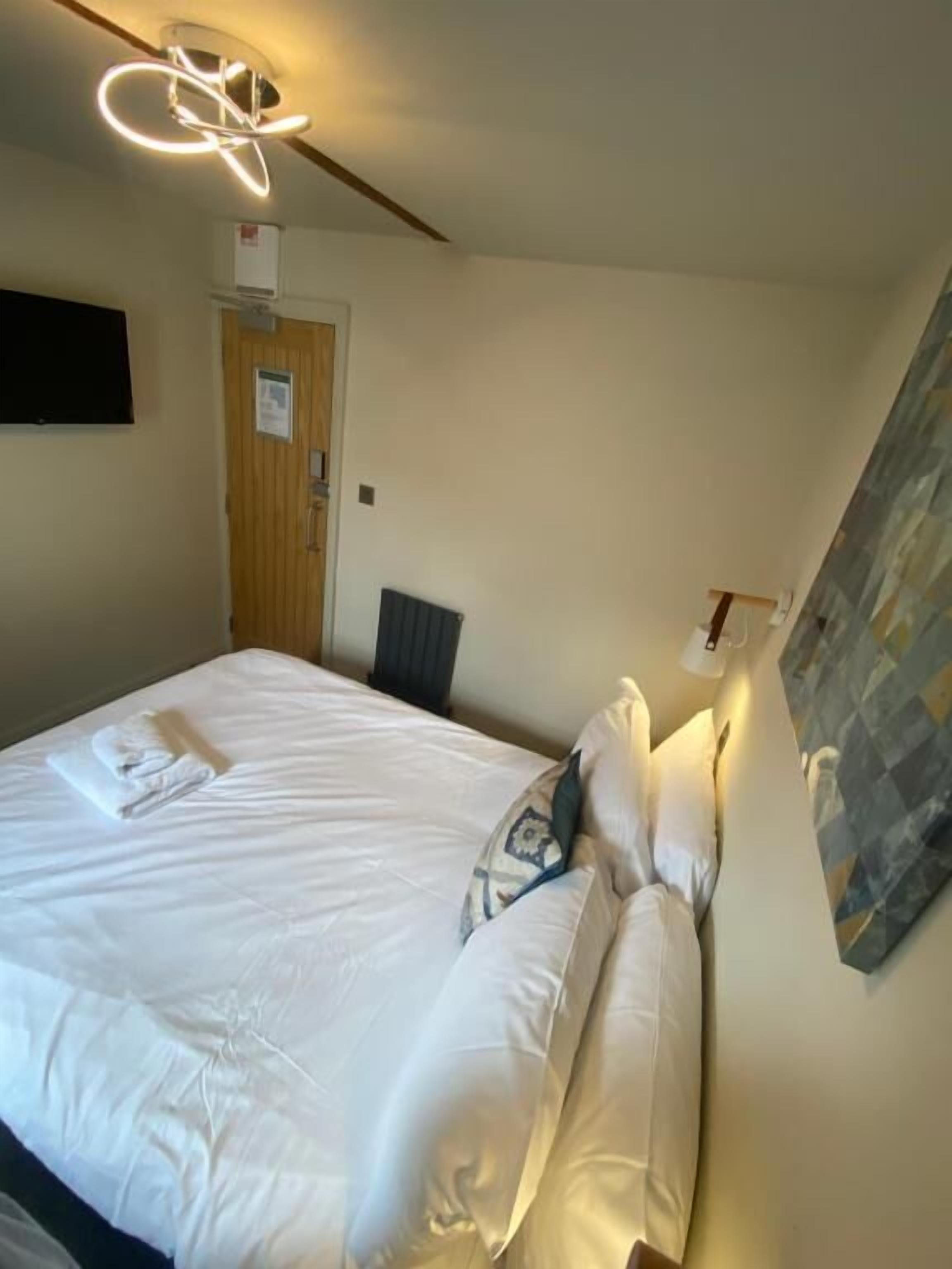 Un lit bien fait, avec du linge de lit blanc et des oreillers, un luminaire moderne au plafond et une porte avec une pancarte.