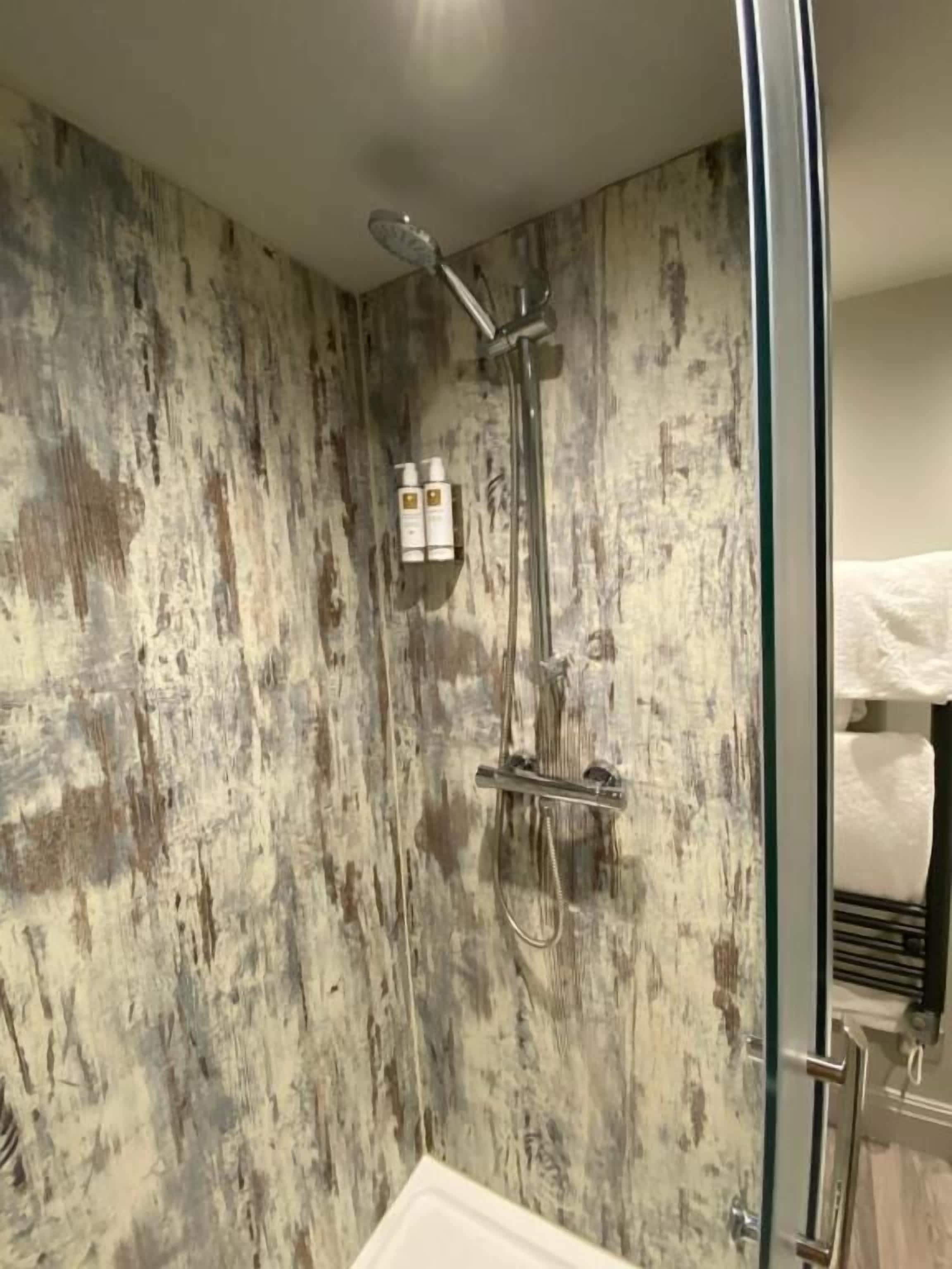 A bathroom with a rustic wall design, a glass shower enclosure, and a visible towel rack.