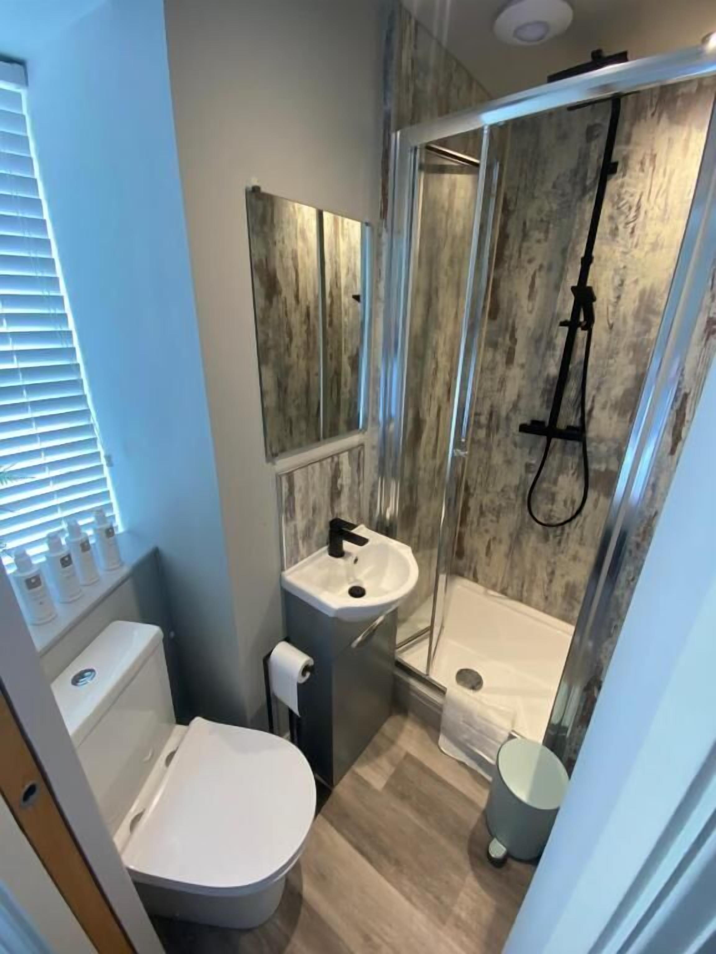 A compact bathroom with a toilet, sink, and glass-enclosed shower.