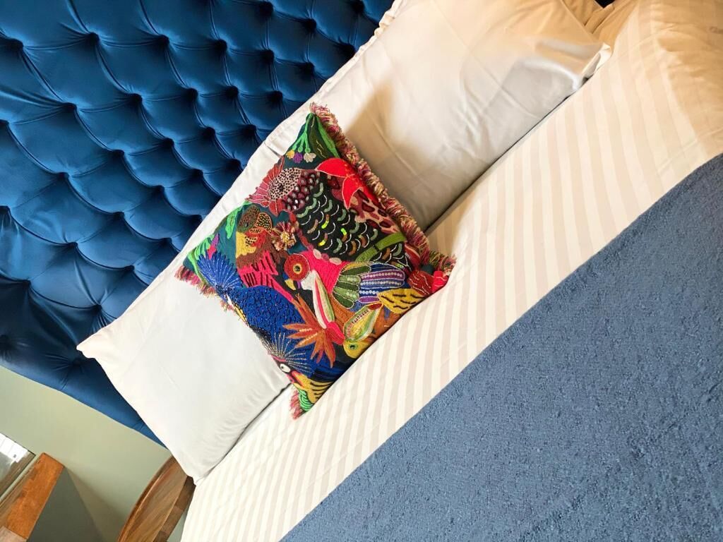 A bed with a tufted headboard, a colorful pillow, and a striped pillow.