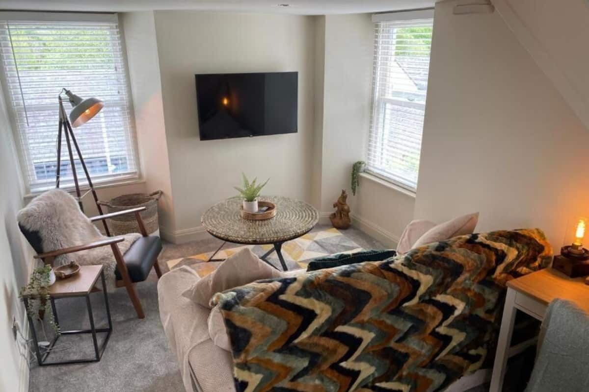 Una sala de estar acogedora con un sofá, una mesita redonda, una lámpara de pie y un televisor fijado en la pared.