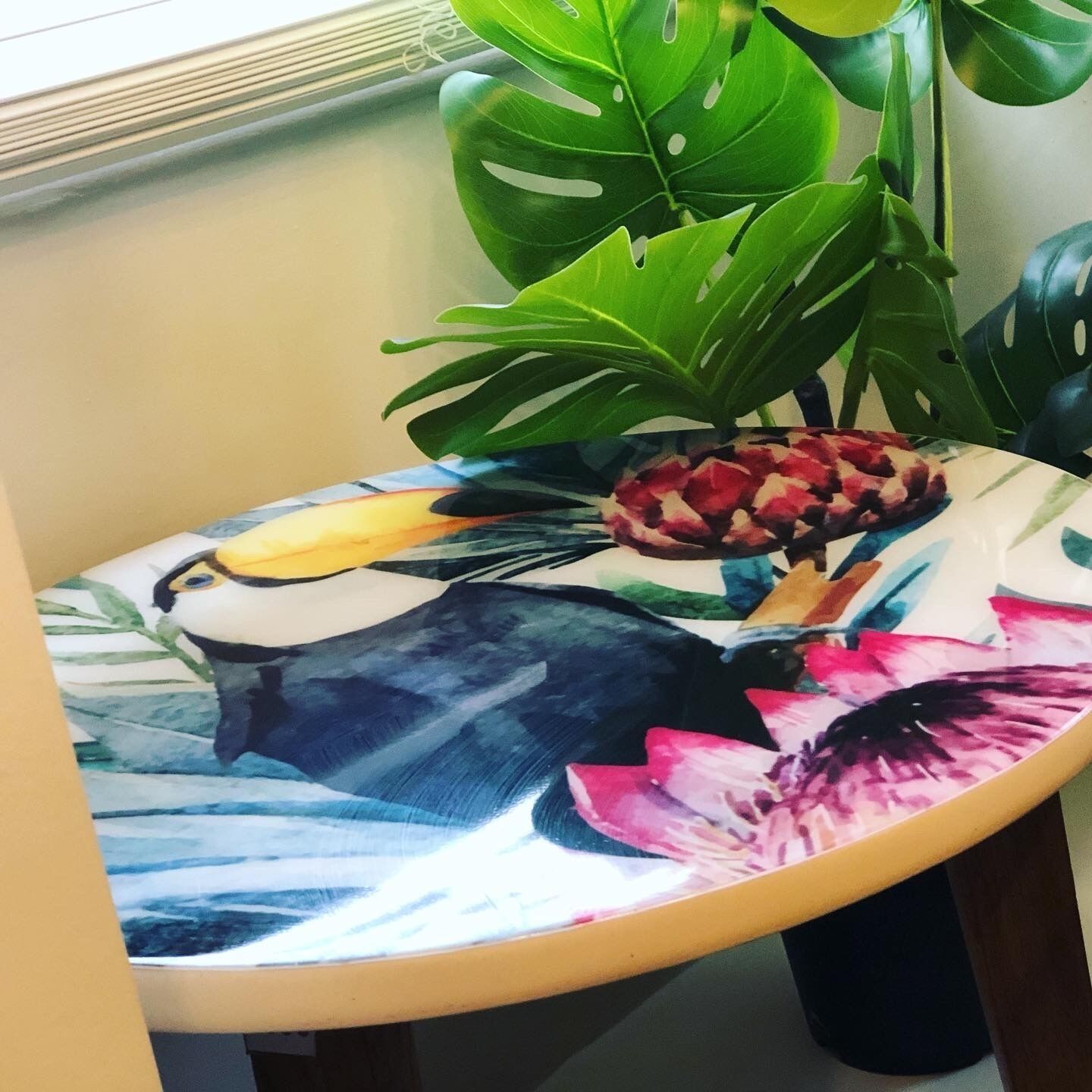 A table with a colorful floral design, a bird illustration, and a plant with large green leaves.