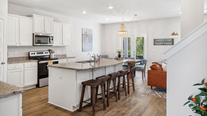 Une cuisine moderne avec des meubles blancs, un îlot central doté de tabourets, un four à micro-ondes et une cuisinière.