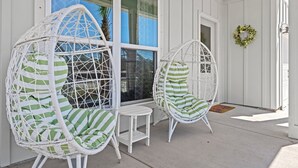 Une véranda avec deux fauteuils en osier blanc dotés de coussins verts, une petite table blanche et une porte ornée d’une guirlande verte.