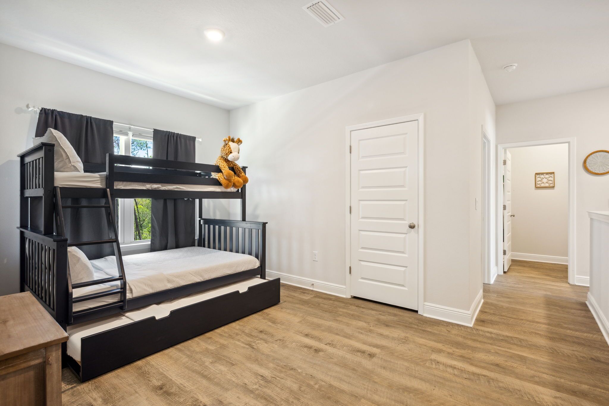 A bunk bed room with a window, a door, and a wooden floor.