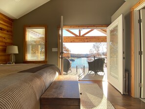 Une chambre à coucher comprenant un lit, une table de chevet, une lampe et donnant sur un balcon avec des chaises et une table.