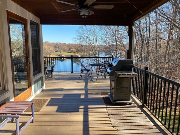 Une terrasse en bois avec un barbecue, des chaises et une vue sur un lac.