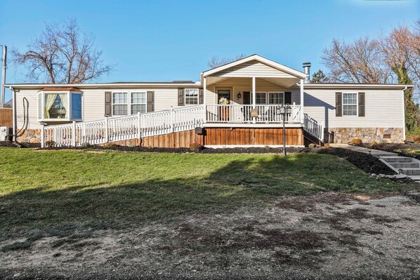A two-story mobile home with a covered porch and a fenced deck.