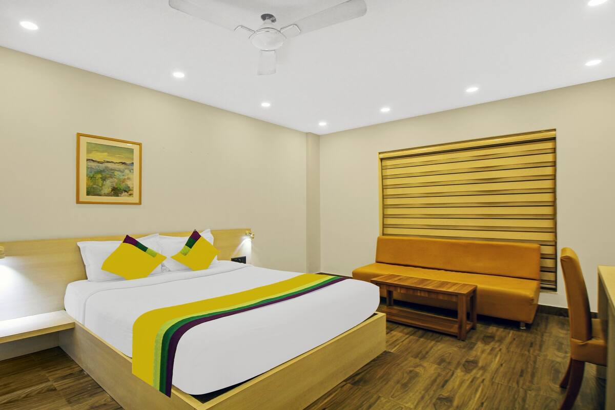 A hotel room with a bed, a bedside table, a chair, a wooden headboard, and a ceiling fan.