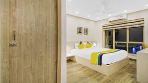 A hotel room with a wooden door, a bed with a colorful blanket, a window with a view, and an air conditioning unit. - Itsy Hotels Transit Express Near Sealdah Station (Kolkata)