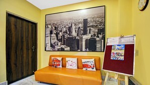A lobby with a large cityscape poster, a wooden door, an orange sofa with themed cushions, and a bulletin board with a poster. - Itsy Hotels Transit Express Near Sealdah Station (Kolkata)