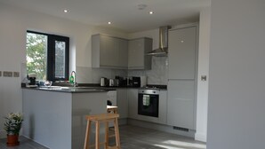 A modern kitchen with white cabinets, a wooden stool, a built-in oven, and a window with blinds.