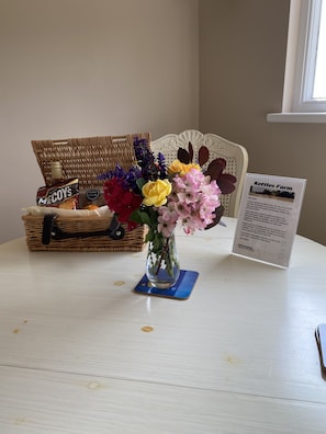 A table with a vase of flowers, a wicker basket with snacks, and a welcome sign.