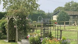 Puutarha, jossa on puinen pergola, metallinen säleikkö ja erilaisia kukkivia kasveja.