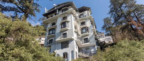 Un edificio de varios pisos con balcones, rodeado de árboles.