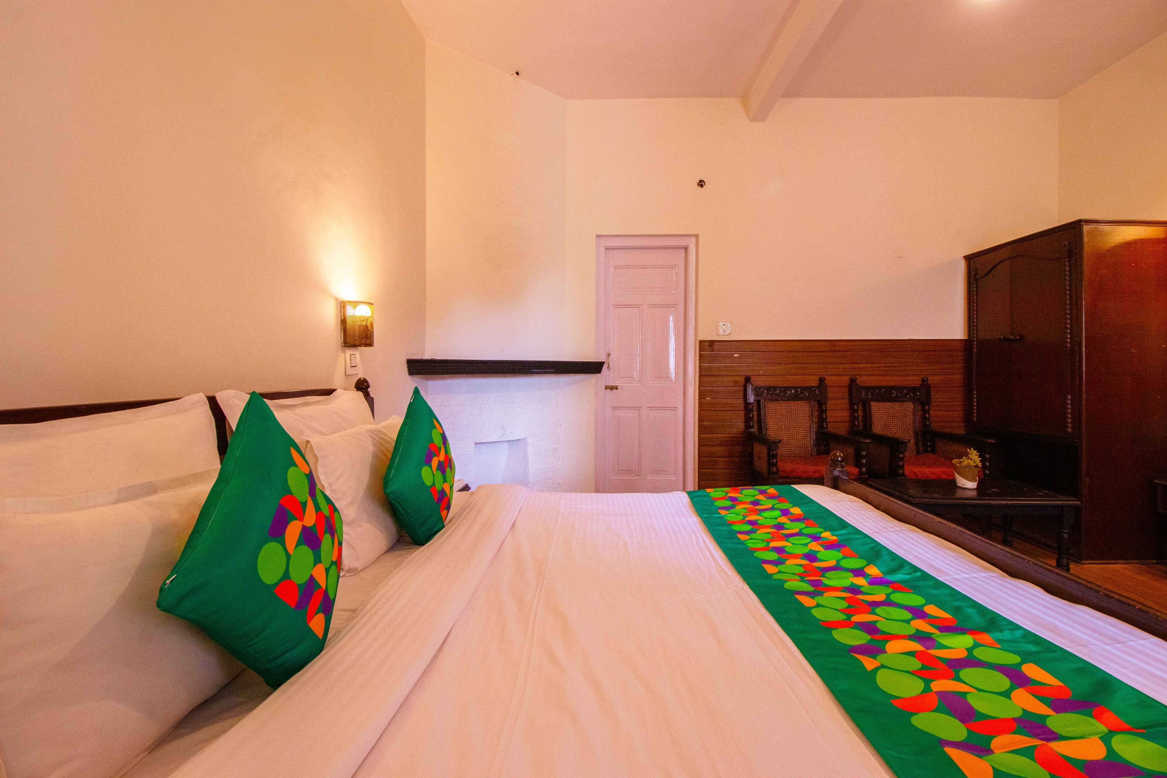 Een hotelkamer met een bed, kussens, een nachtkastje, een spiegel en een deur.