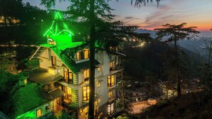 A multi-story building with balconies, a green-lit roof, and a view of the surrounding landscape. - Treebo The Alpine Heritage Residency (Shimla)