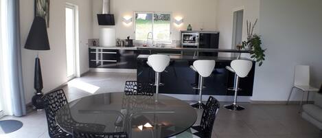 A modern kitchen with a central island, black and white bar stools, and a dining table with chairs.