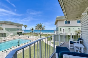 A balcony with a pool, lounge chairs, and a view of the ocean.