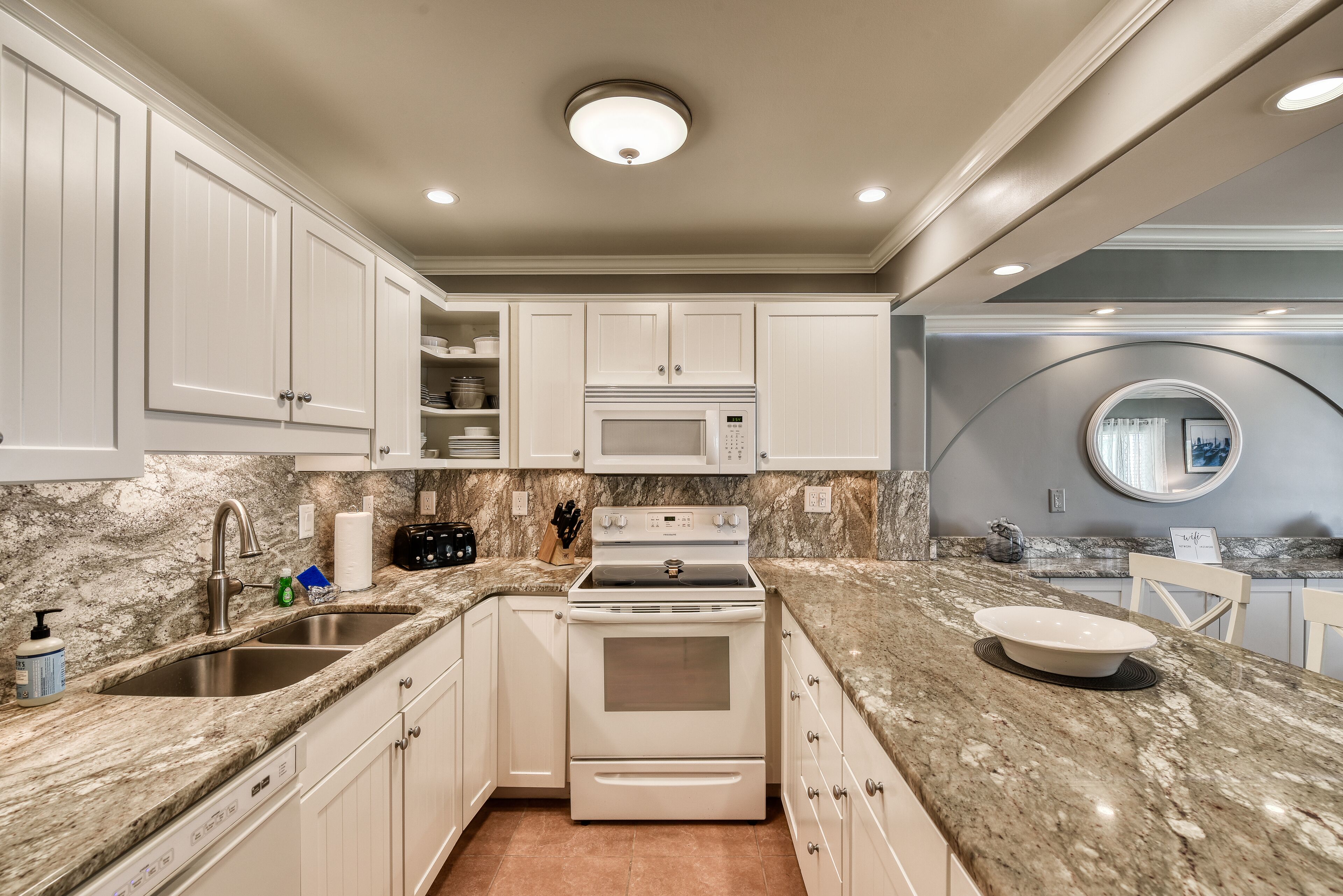 A kitchen with white cabinetry, a built-in microwave, a stove, and a granite countertop.