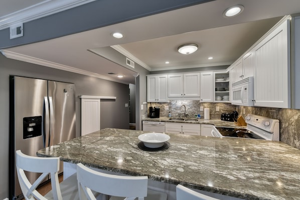A modern kitchen with granite countertops, stainless steel appliances, white cabinetry, and recessed ceiling lighting.