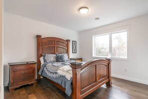 Un dormitorio con una cama de madera, una mesita de noche, un aparador y una ventana con vistas a árboles.