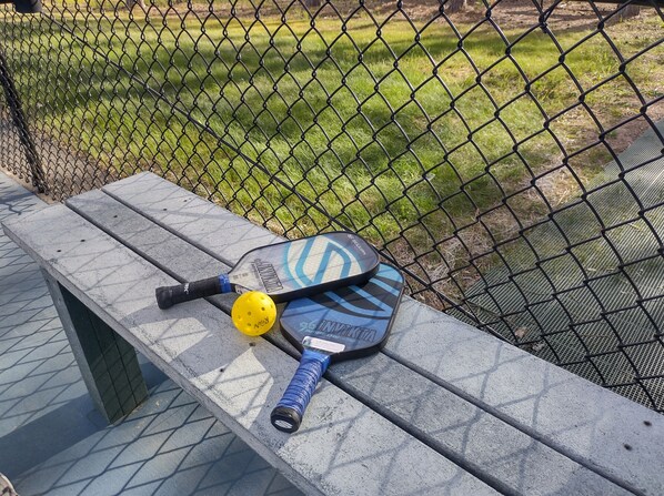 A cricket bat and ball on a bench near a chain-link fence.