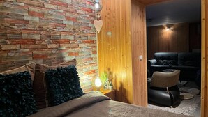 A bedroom with a brick-patterned wall, a wooden door, a bed with dark blue pillows, and a small table with a lamp. - Cosy, pet Friendly Apartment in Portula, Italy (Portula)