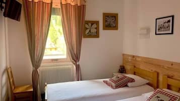 Una habitación con dos camas individuales, cabecera de madera, radiador, una silla y una ventana con cortinas.