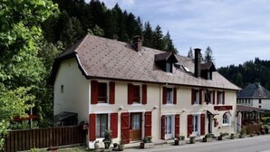 A two-story building with a sloped roof, red shutters, and a row of potted plants along the front. - Ô Caprice du Guiers (Saint-Pierre-de-Chartreuse)