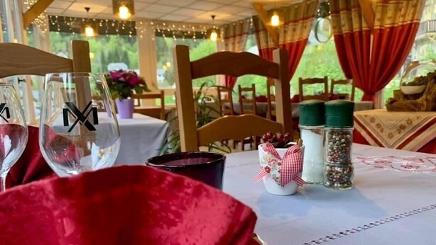 A table set for dining with a red tablecloth, a glass with a logo, a small decorative pot, and salt and pepper shakers. - Ô Caprice du Guiers (Saint-Pierre-de-Chartreuse)