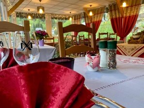 Una mesa dispuesta para comer, con mantel rojo, un vaso con un logotipo, una pequeña maceta decorativa y saleros y pimenteros.