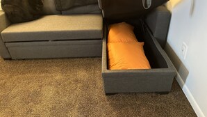 A grey sofa with a storage compartment containing an orange pillow.