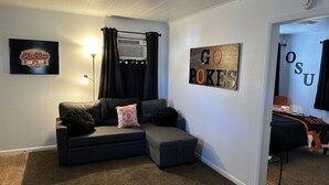 A modern living room with a sectional sofa, a ceiling fan, and a wall-mounted air conditioner.