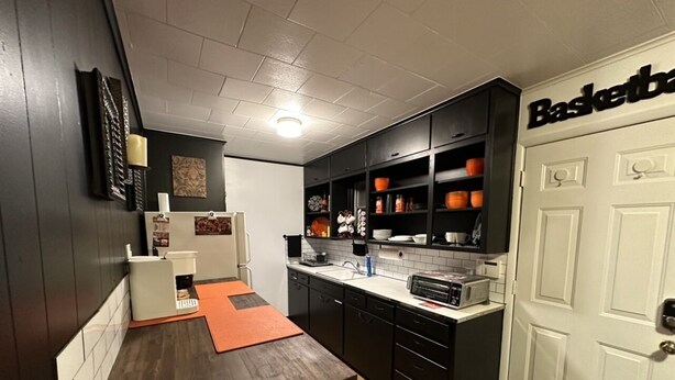 A compact kitchen with dark cabinetry, a white door labeled "Basketball," and a small dining area with a wooden table and orange rug.