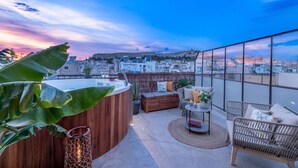 Eine Dachterrasse mit Whirlpool, Korbmöbeln und Blick auf die Stadt bei Sonnenuntergang.