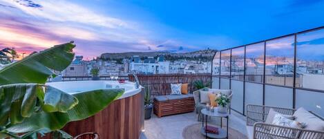 Eine Dachterrasse mit Whirlpool, Korbmöbeln und Blick auf die Stadt bei Sonnenuntergang.