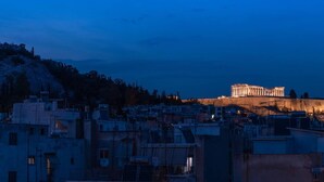 Eine Stadtansicht mit einem markanten, antiken griechischen Tempel im Hintergrund, umgeben von Wohnhäusern.