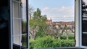 A window with a view of a town, including buildings and trees.