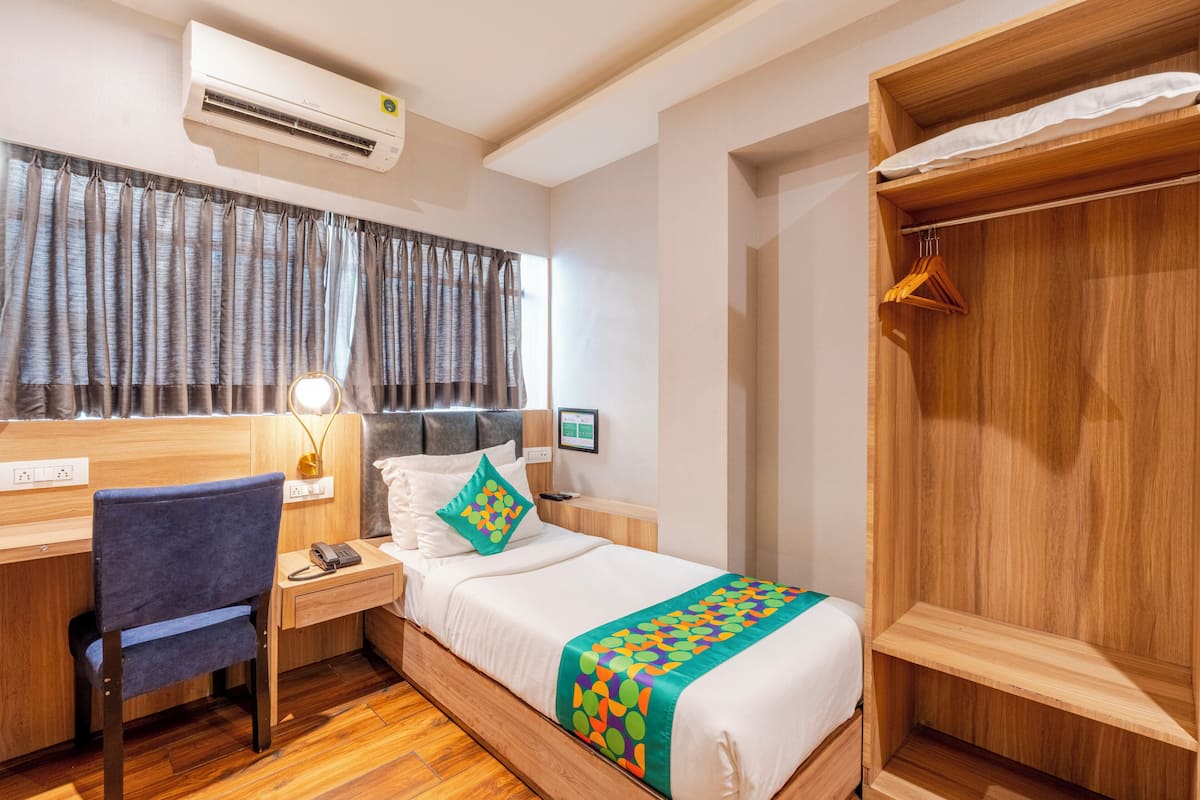 Una habitación de hotel con un escritorio de madera, una cama con una manta colorida, un armario y un equipo de aire acondicionado.