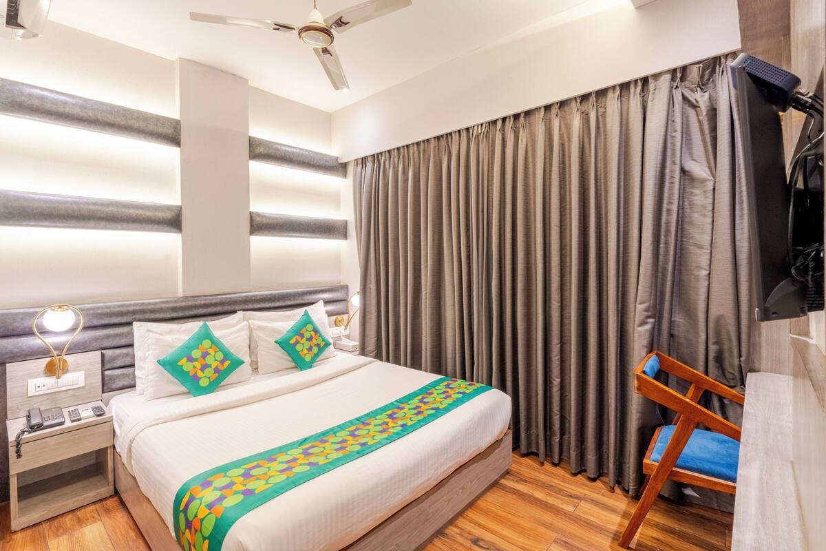 Habitación de hotel con cama, escritorio con teléfono, silla, ventilador de techo y televisor montado en la pared.