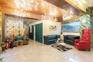 A lobby with a green sofa, a red armchair, a black leather sofa, a gold-framed coffee table, and a patterned wall.