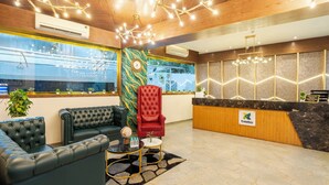 A modern reception area with a wooden ceiling, a red chair, a black leather sofa, a reception desk, and a large window. - Treebo Premium Widlor Boutique (Mumbai)