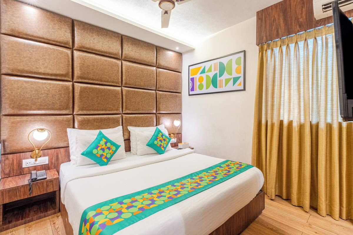 Una habitación de hotel con una cama grande, un cabecero, una mesita de noche con lámpara, un teléfono y un televisor.