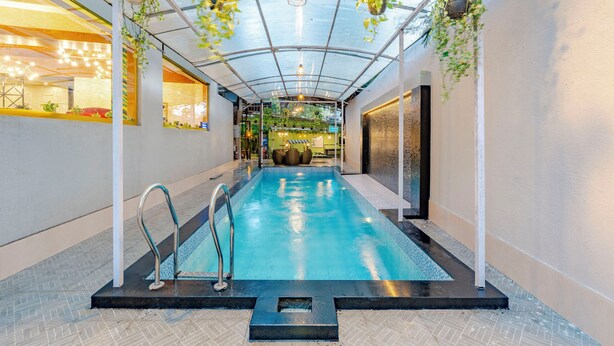 An indoor swimming pool with a glass ceiling, metal railings, and hanging plants. - Treebo Premium Widlor Boutique (Mumbai)