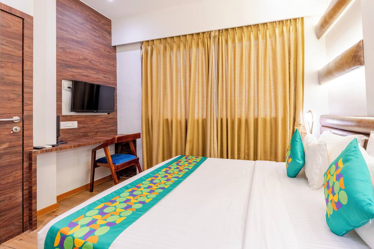Habitación de hotel con cama, escritorio, televisión y un ventanal con cortinas.